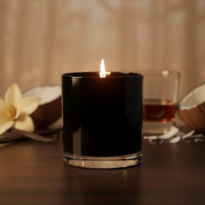Black candle in a glass holder with a blurred background featuring flowers and a glass of liquid.
