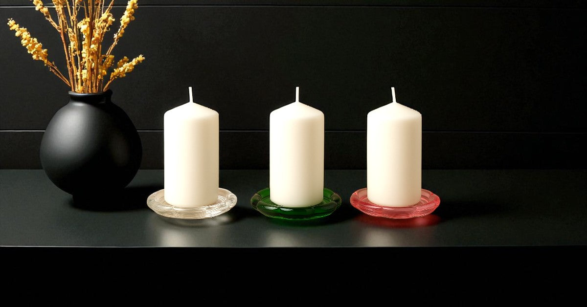 Four white candles on colorful holders with a black vase containing dried flowers against a black background.