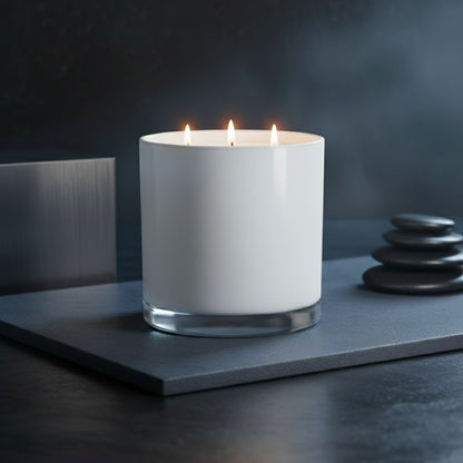 White candle in a glass container on a dark surface with stones in the background