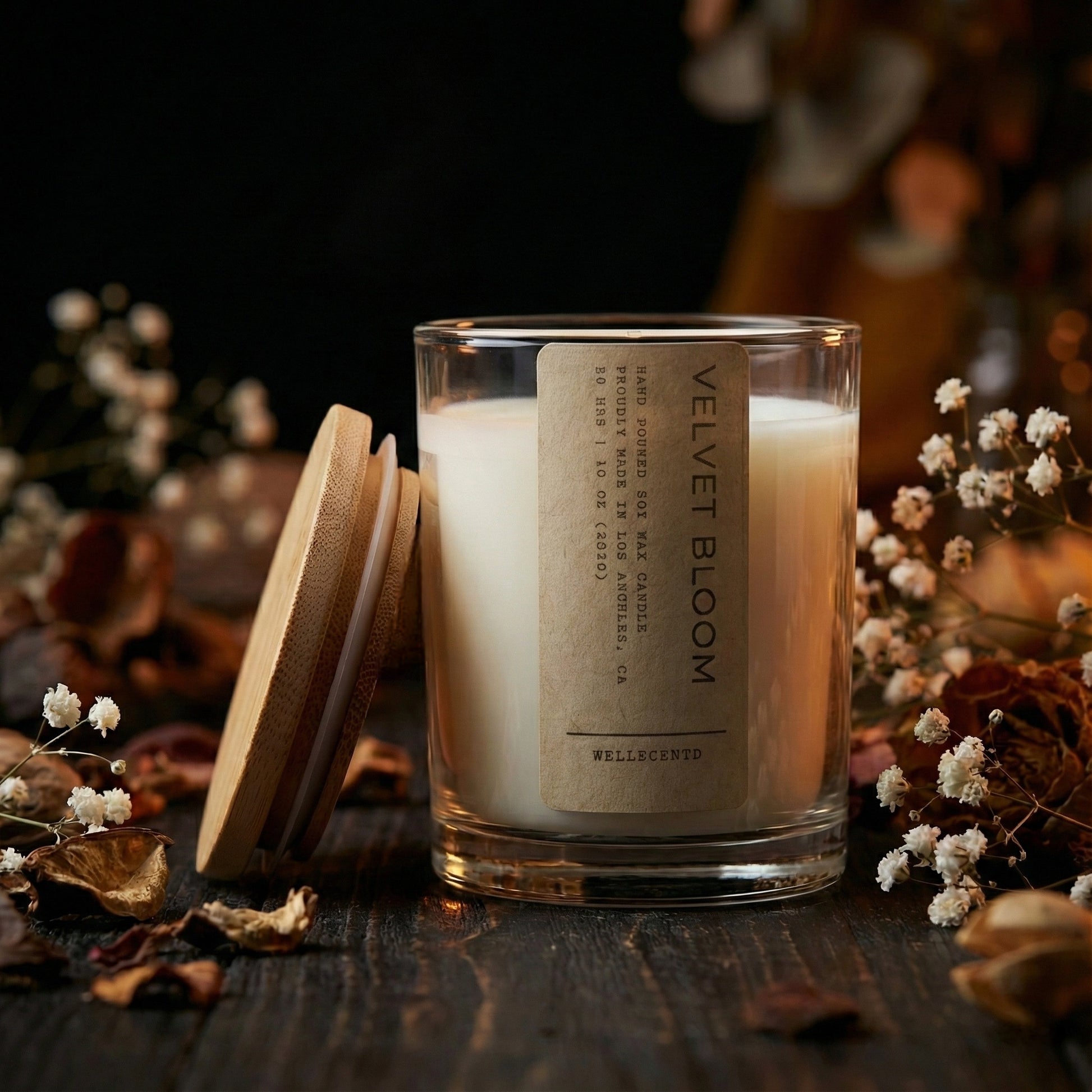 Candle with a label on a wooden surface surrounded by flowers
