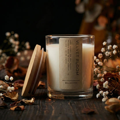 Candle with a label on a wooden surface surrounded by flowers