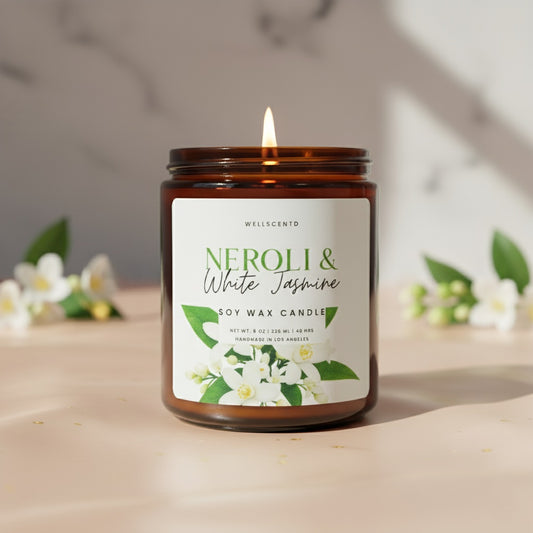 Wellscentd Neroli & White Jasmine Candle in amber glass jar with soft flame, jasmine blossoms, and marble background.