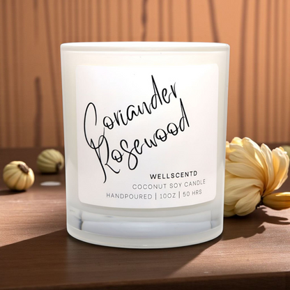 Frosted candle with 'Coriander Rosewood' label on a wooden surface with decorative elements.