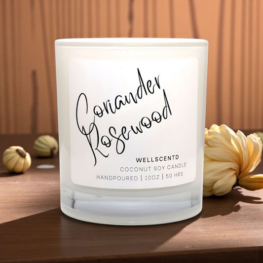 Frosted candle with 'Coriander Rosewood' label on a wooden surface with decorative elements.