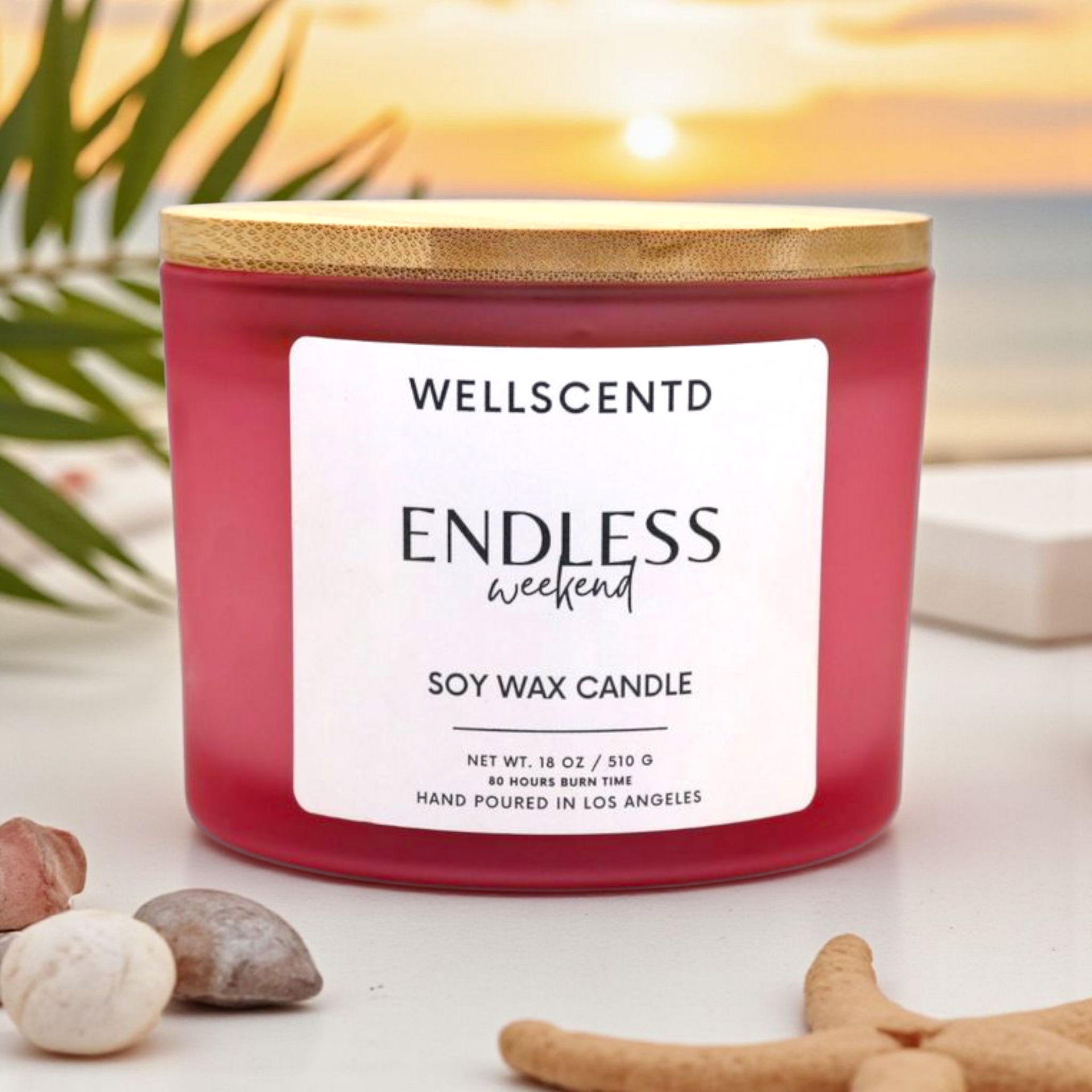 Pink soy wax candle labeled 'Endless Weekend' by Wellscentd on a surface with decorative elements.